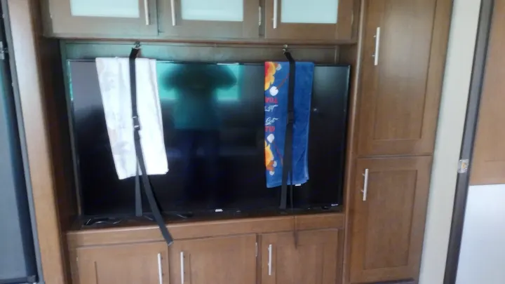 RV rental interior: TV secured for travel by hanging towels and straps within built-in wooden cabinets.. Avenger ATI 2019
