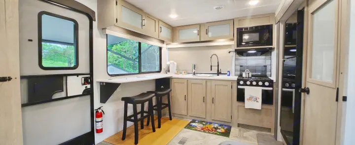 Modern RV rental's inviting kitchen & living area with full appliances, window bar, and entryway, perfect for trips.. Forest River Wildwood Platinum 2024