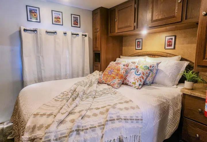 Cozy RV rental bedroom with a large bed, colorful pillows, throw blanket, wall art, and built-in storage.. Forest River Coachmen Leprechaun 2015