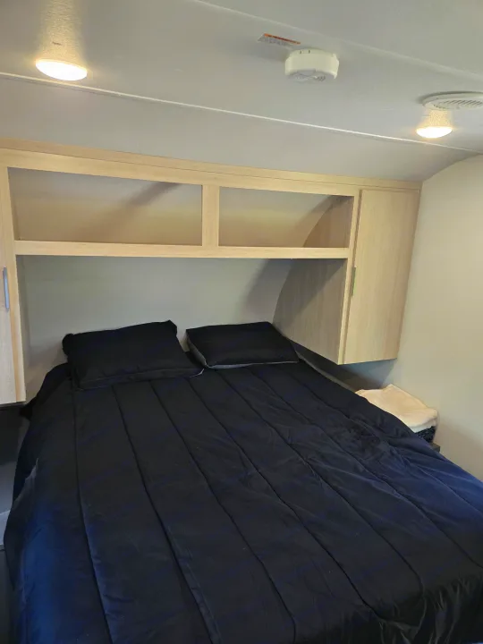 RV rental bedroom with black bedding, light wood overhead storage, and a smoke detector on the ceiling.. Prime Time Tracer LE 2024