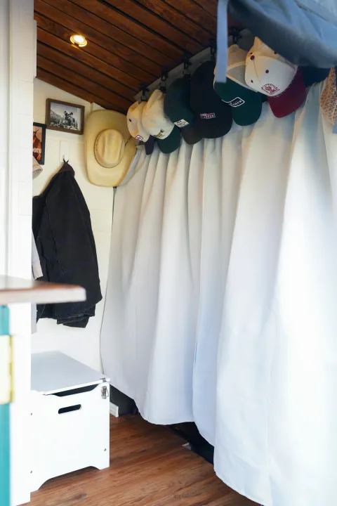 Cozy RV rental interior shows wooden ceiling, white walls, storage bench, and organized hats and jackets.. Ford Transit Custom 2022