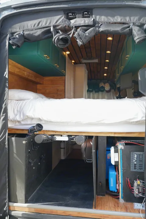 This RV rental shows a well-organized camper interior with a cozy bed, under-bed storage, and accessible electrical systems.. Ford Transit Custom 2022