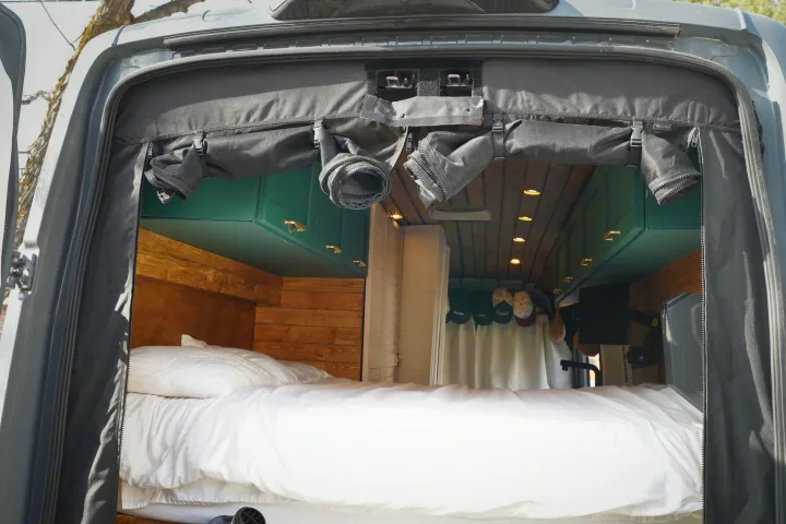 RV rental interior showcasing a comfortable bed, custom teal cabinets, and wood paneling.. Ford Transit Custom 2022