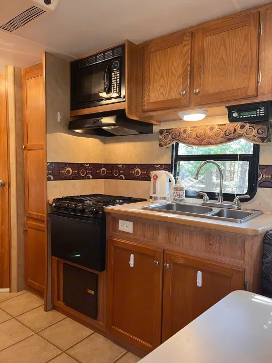 RV rental kitchenette with stove, microwave, double sink, warm wood cabinets, and bright window.. R-Vision Trail Sport 2014