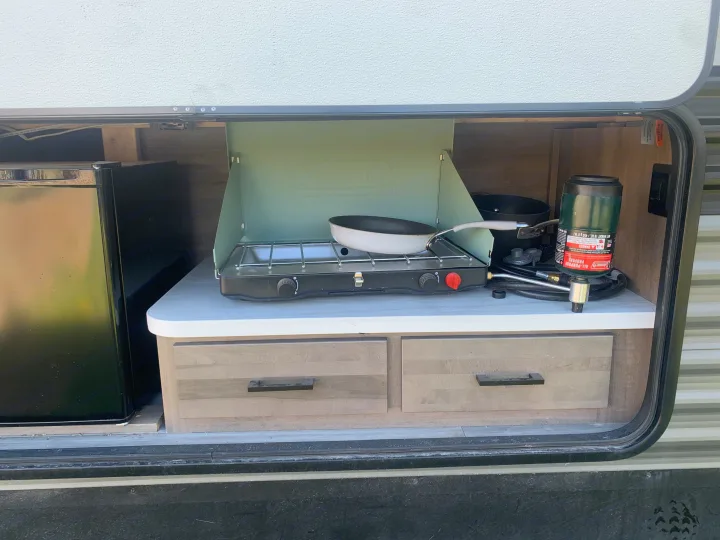 RV rental outdoor kitchen featuring a Coleman propane stove, pan, and mini-fridge. Perfect for camping cooking convenience.. Jayco Jay Flight 2024