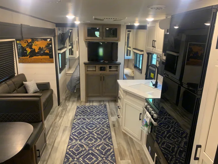 This modern RV rental interior boasts a full kitchen, living area with a dinette & sofa, TV console, and visible bunk beds.. Jayco Jay Flight 2024