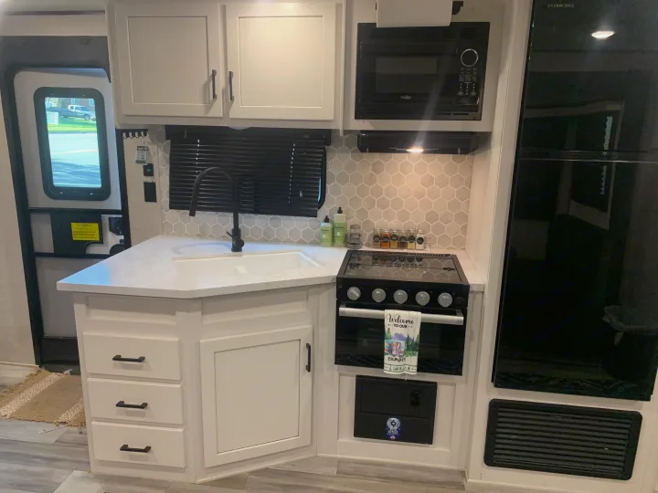 Inside a clean RV rental kitchen: white cabinets, black appliances, hexagon backsplash, and all essentials.. Jayco Jay Flight 2024