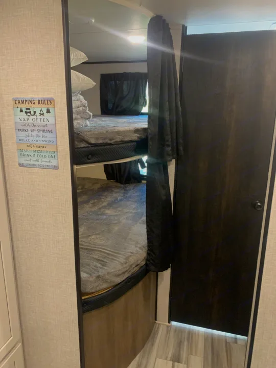 Inside an RV rental: comfy bunk beds with privacy curtains & a fun "Camping Rules" sign. Ideal for camping trips.. Jayco Jay Flight 2024