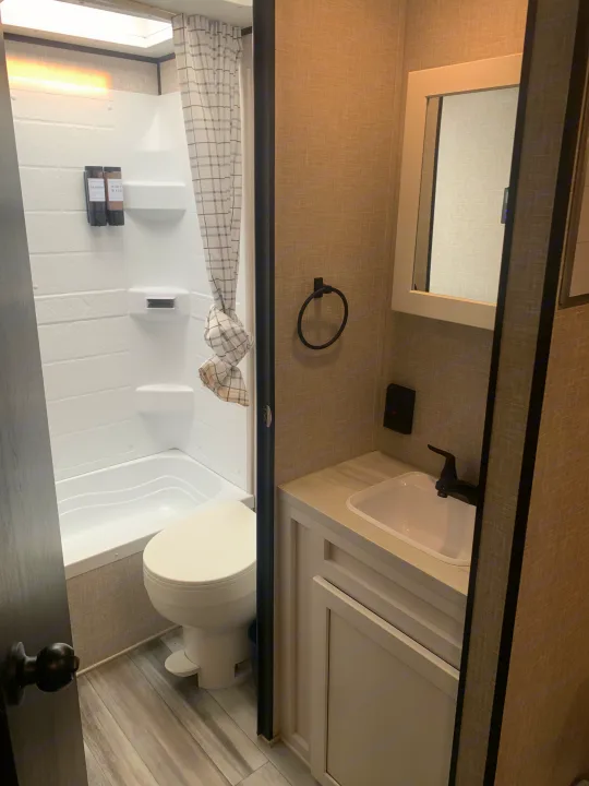 This modern RV rental bathroom features a white shower/tub, toilet, and light-toned vanity with a black faucet.. Jayco Jay Flight 2024