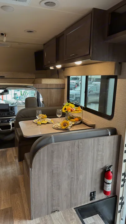 This RV rental features a comfortable dinette with a table set for dining, an overhead bunk, and front cab view.. Winnebago Minnie Winnie 2023