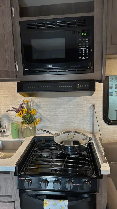 Compact RV rental kitchen with stove, microwave, and sink. Perfect for preparing meals while traveling.. Winnebago Minnie Winnie 2023