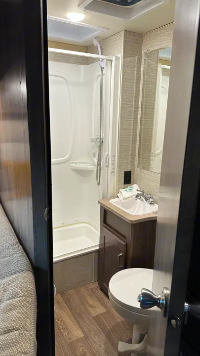 Inside a compact RV rental bathroom: shower, sink vanity, and toilet, efficiently designed for travel.. Winnebago Minnie Winnie 2023