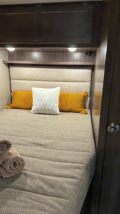An inviting RV rental bedroom with a gray textured bedspread, decorative pillows, and convenient overhead storage.. Winnebago Minnie Winnie 2023