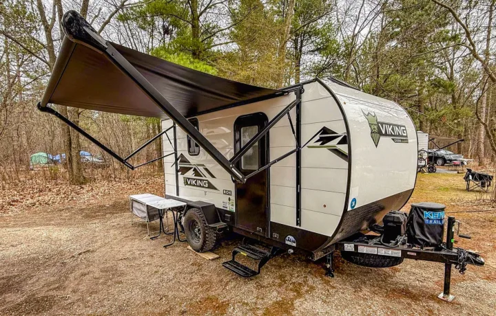 Viking travel trailer RV rental parked at a woodland campsite with awning extended. Perfect for camping.. Coachmen Viking 1200ROK 2025