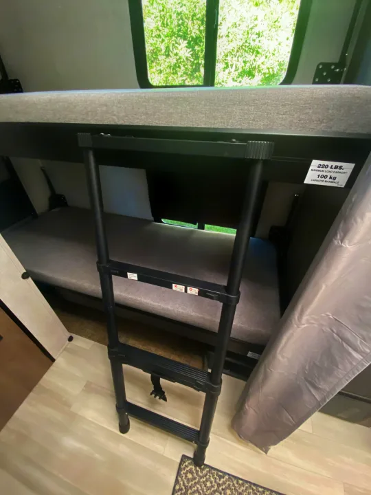 RV rental interior: Bunk beds with a retractable ladder for top bunk access, showing weight limits and a bright window view.. Ford Transit 2023