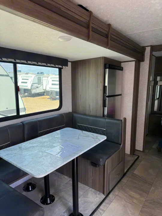 RV rental interior showcasing a cozy dinette with U-shaped seating, a table, and a built-in refrigerator.. Dutchmen Kodiak Ultra Lite 2021