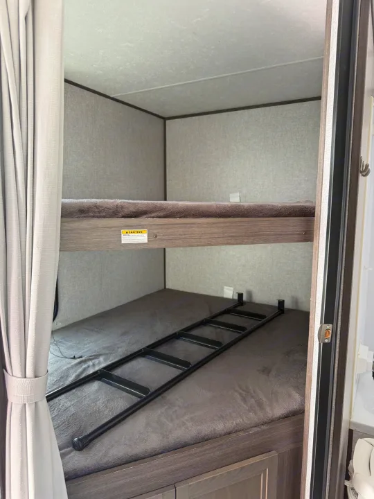 RV rental bunk beds: A cozy sleeping area with two beds, a ladder for access, and light grey privacy curtains.. Dutchmen Kodiak Ultra Lite 2021