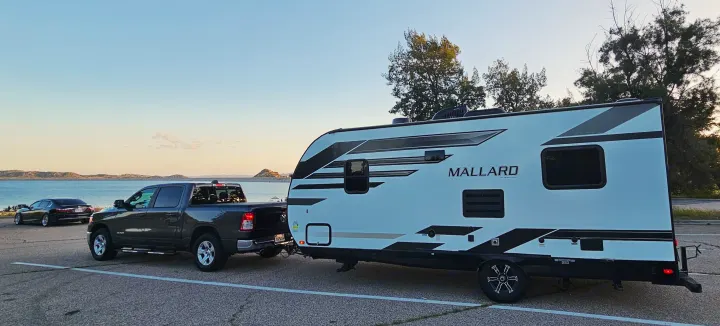 RV rental: A pickup truck towing a "MALLARD" travel trailer by a beautiful lake. Perfect for camping adventures!. Heartland RVs Mallard 2021