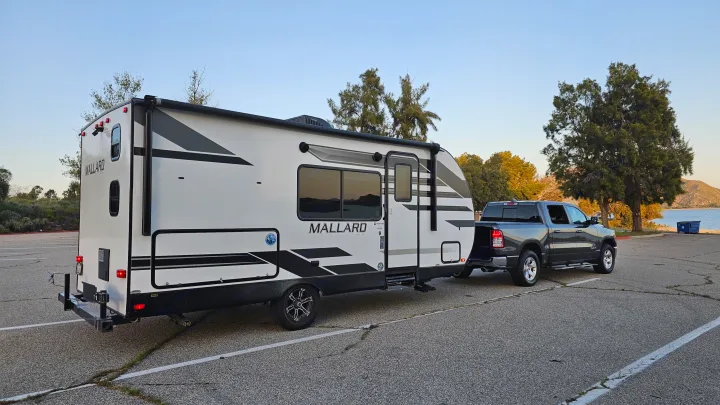 Grey pickup truck towing a white Heartland Mallard rv rental, ready for camping by a scenic lake.. Heartland RVs Mallard 2021