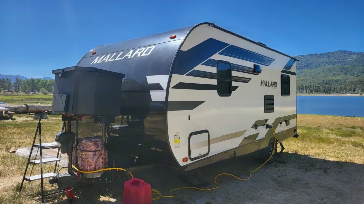 This Mallard RV rental sits by a beautiful lake with mountains under a sunny sky, perfect for outdoor adventures.. Heartland RVs Mallard 2021