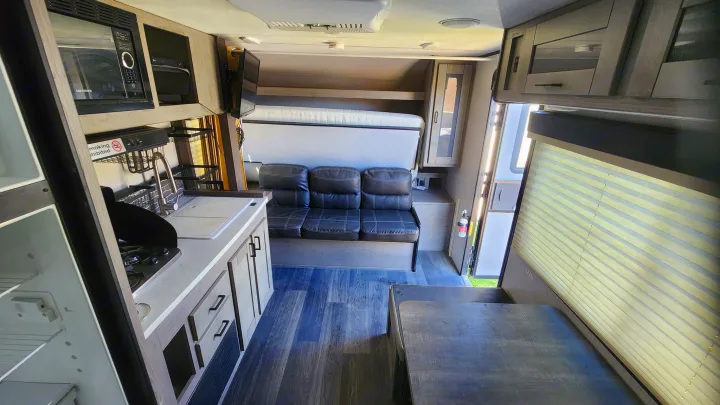 This rv rental interior features a functional kitchen with a microwave, sink, stove, and fridge, plus a sofa, fold-down bed, and dinette table.. Heartland RVs Mallard 2021