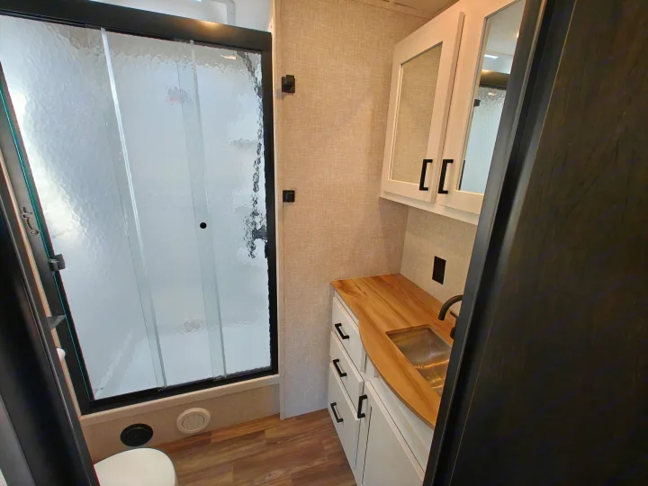 Modern RV rental bathroom: compact shower, vanity with sink, and white cabinets.. Highland Ridge Open Range Light 2024