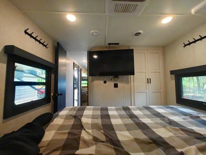 Cozy RV rental bedroom with TV, plaid bed, and windows. Ideal for travel.. Highland Ridge Open Range Light 2024