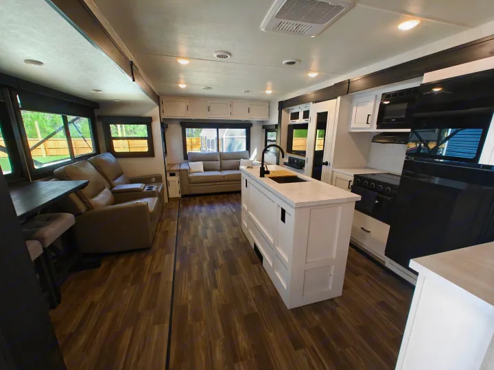 Modern RV rental interior showing living room with recliners & sofa, plus kitchen with island & appliances.. Highland Ridge Open Range Light 2024