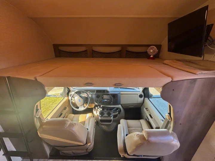 RV rental interior featuring an overhead bunk bed, entertainment TV, and the driver's cockpit with seating.. Jayco Redhawk 2018