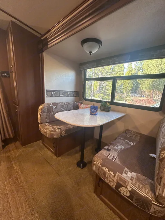 Cozy RV rental interior featuring a spacious dinette, large window with a forest view, and comfortable seating for travelers.. Jayco White Hawk Ultra Lite 2015