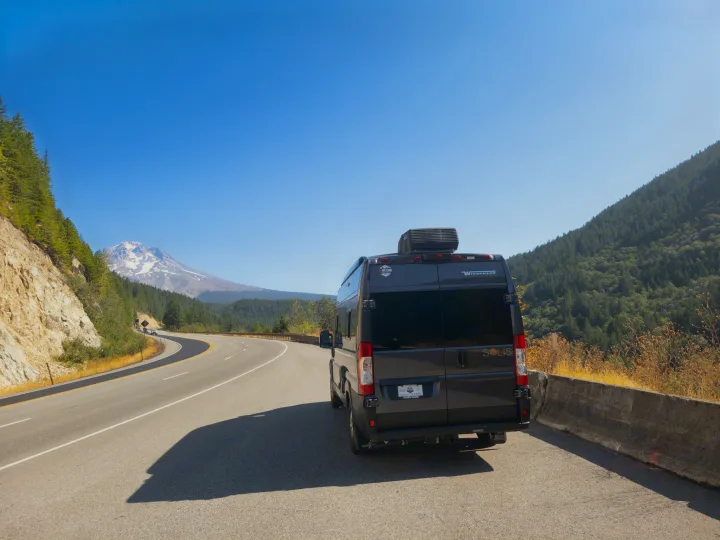 An RV rental Winnebago Solis camper van on a scenic highway with snow-capped Mt. Hood in the distance.. Winnebago Solis 2023