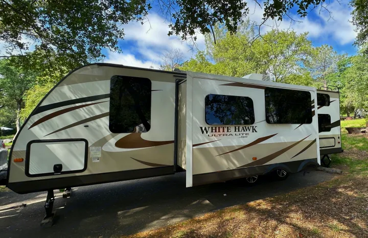 White Hawk Ultra Lite RV rental set up at a wooded campsite. Its slide-outs are extended, ready for a spacious stay.. Jayco White Hawk Ultra Lite 2015