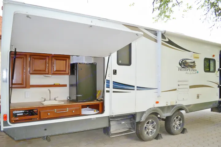 This RV rental features a convenient outdoor kitchen with a sink, fridge, and cabinets, perfect for camping adventures.. Coachmen Freedom Express 2013