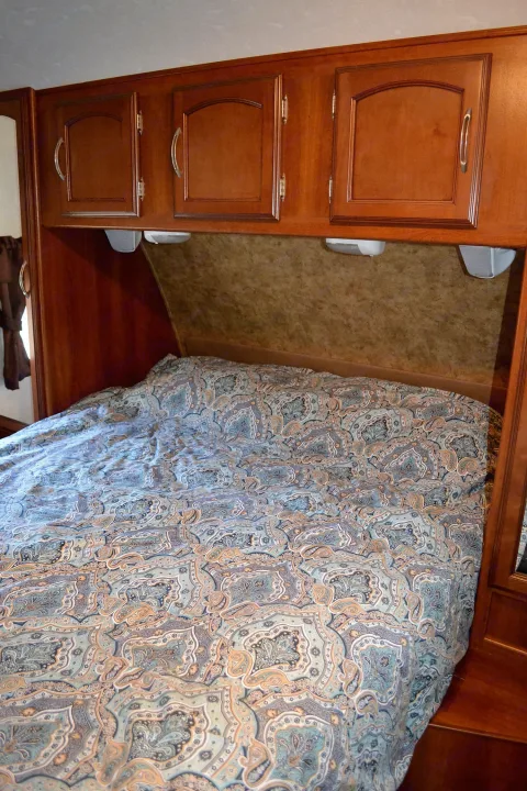 RV rental interior with a bed featuring a paisley comforter, overhead wooden cabinets, and built-in storage.. Coachmen Freedom Express 2013