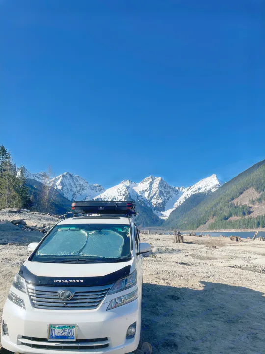 White RV rental van facing snow-capped mountains, a lake, and a dry bed. Scenic BC outdoor adventure awaits!. Toyota Dreamseeker Voyager 2008