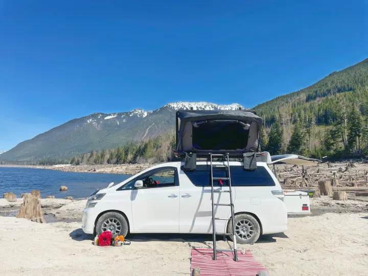 Lakeside white van with roof tent setup; a great RV rental for scenic outdoor camping. Mountains & stumps.. Toyota Dreamseeker Voyager 2008