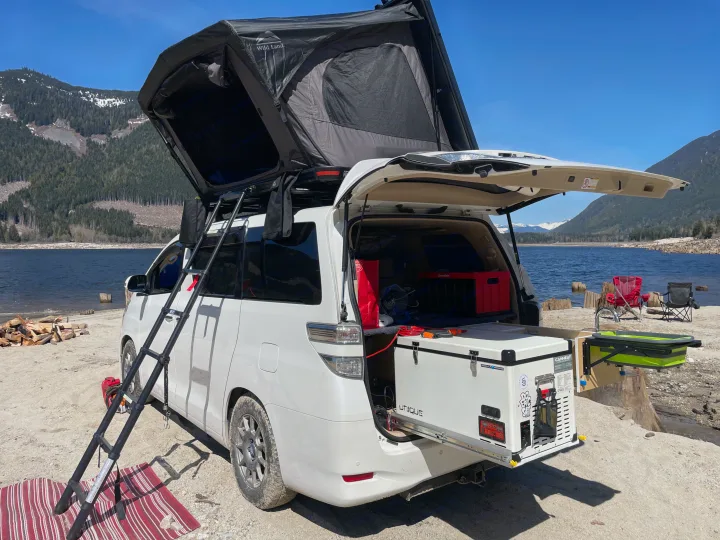 Ultimate RV rental setup: white camper van with deployed rooftop tent, ready for lakeside mountain camping.. Toyota Dreamseeker Voyager 2008