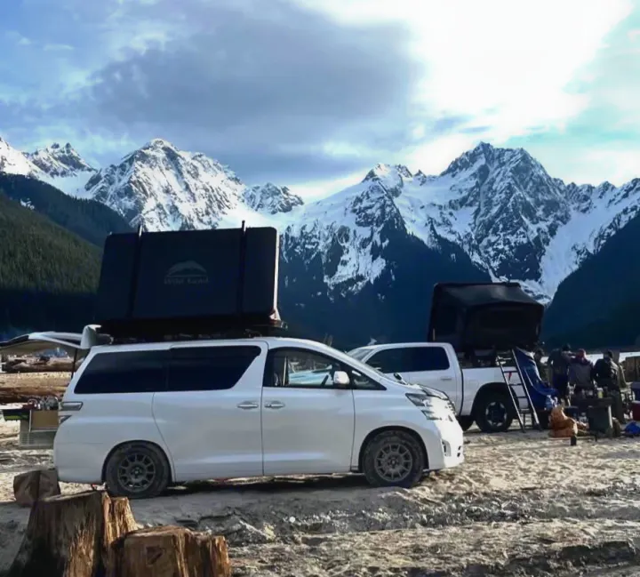 Rooftop tent RV rental: white van & truck camping by majestic snowy mountains. Group enjoys outdoor adventure.. Toyota Dreamseeker Voyager 2008