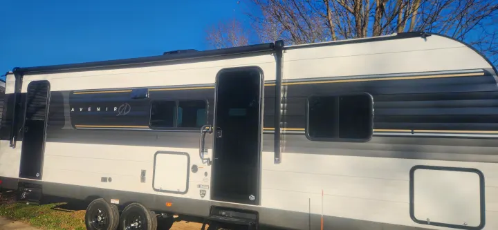 Sleek Avenir RV rental with a striking white & black exterior, gold accents, and multiple windows, parked outdoors.. Cruiser RV Avenir 2024
