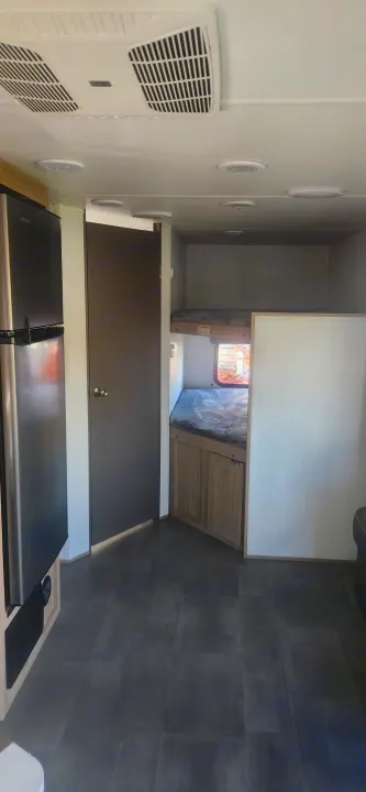 RV rental interior: fridge, private door, and two bunk beds. Features dark flooring and ceiling AC.. Cruiser RV Avenir 2024