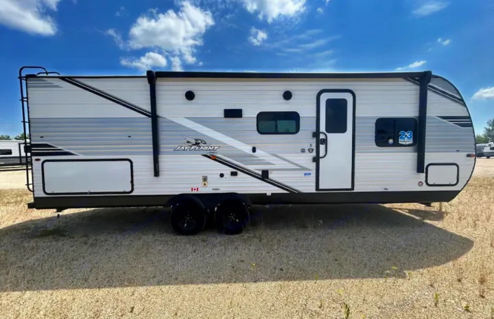 This white & grey Jay Flight travel trailer, an excellent RV rental option, is shown from its side exterior on a gravel lot.. Jayco 267BHS 2025