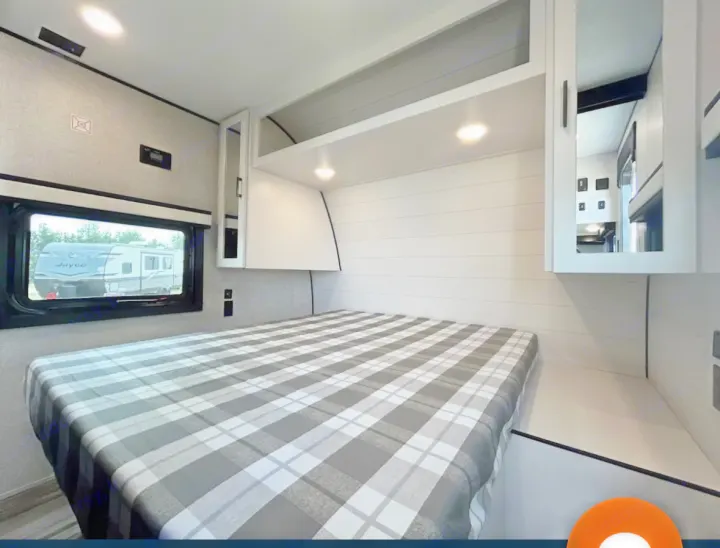 Experience comfort in this modern RV rental bedroom. Features a plaid bed, cabinets, and a window view, ideal for your next trip.. Jayco 267BHS 2025