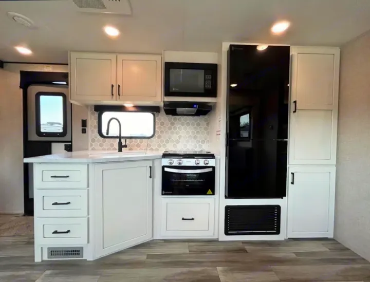 Clean, modern RV kitchen perfect for an rv rental. Features white cabinets, light counters, black appliances, & hex tile backsplash.. Jayco 267BHS 2025