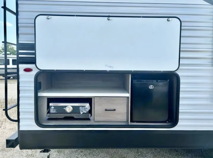 An RV rental reveals its outdoor kitchen: a pull-out grill, drawer, and mini-fridge within an open exterior compartment.. Jayco 267BHS 2025