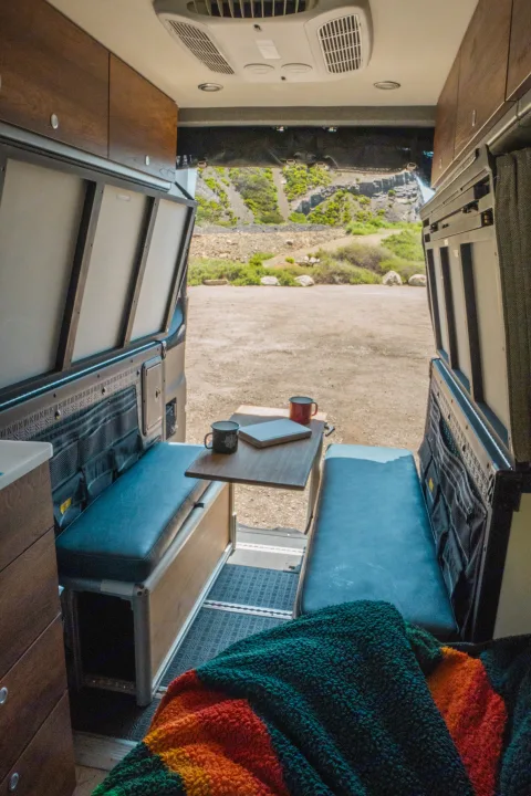 This RV rental offers a spacious interior with benches, table, and a scenic view of rocky hills and vegetation.. Storyteller Overland Storyteller Overland Class B 2022