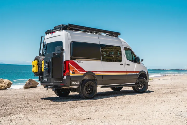 White Storyteller Overland RV rental van, equipped for adventure, parked on a beach with the ocean visible.. Storyteller Overland Storyteller Overland Class B 2022
