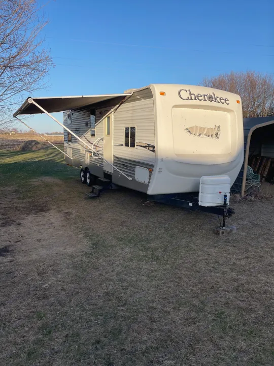A beige Cherokee travel trailer with its awning extended, parked on dry grass. Great option for an RV rental adventure!. Forest River Cherokee 2008