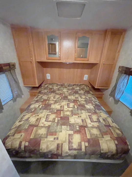 Cozy RV rental bedroom with a patterned comforter, overhead cabinets, and windows, ready for a comfortable stay.. Forest River Cherokee 2008