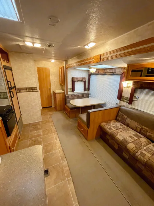 Bright RV rental interior showing a kitchen, booth dinette, and living room with brown sofa and wood accents.. Forest River Cherokee 2008