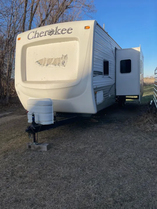 White Cherokee RV rental trailer with extended slide-out, parked on dry grass, ready for adventure.. Forest River Cherokee 2008